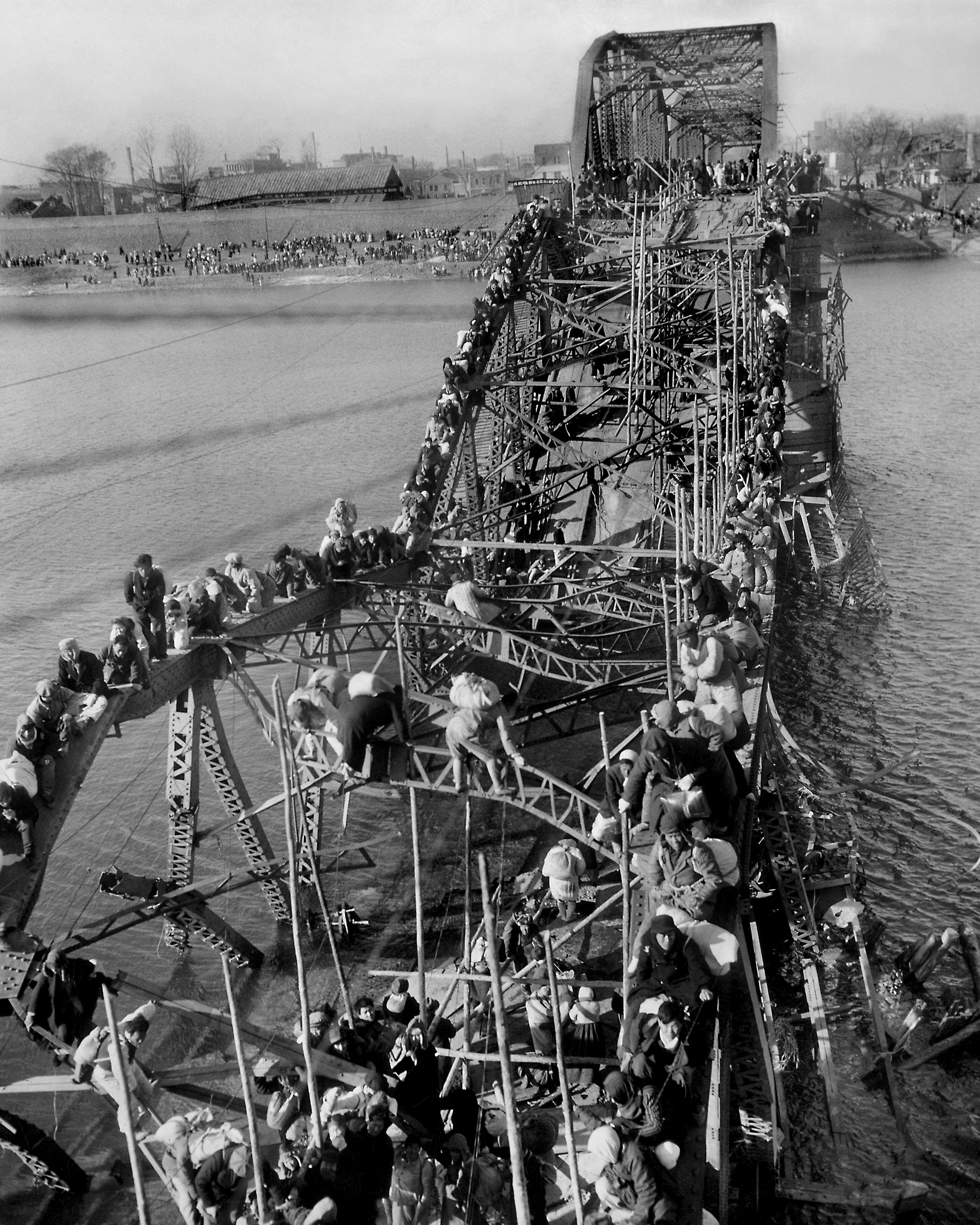 In bitter cold, residents from Pyongyang, North Korea, and refugees of other areas crawl over precarious, tangled girders of a bridge across the Taedong River on Dec. 4, 1950, as they flee south ahead of advancing Chinese Communist troops fighting on the side of North Korea. (AP Photo/Max Desfor)
