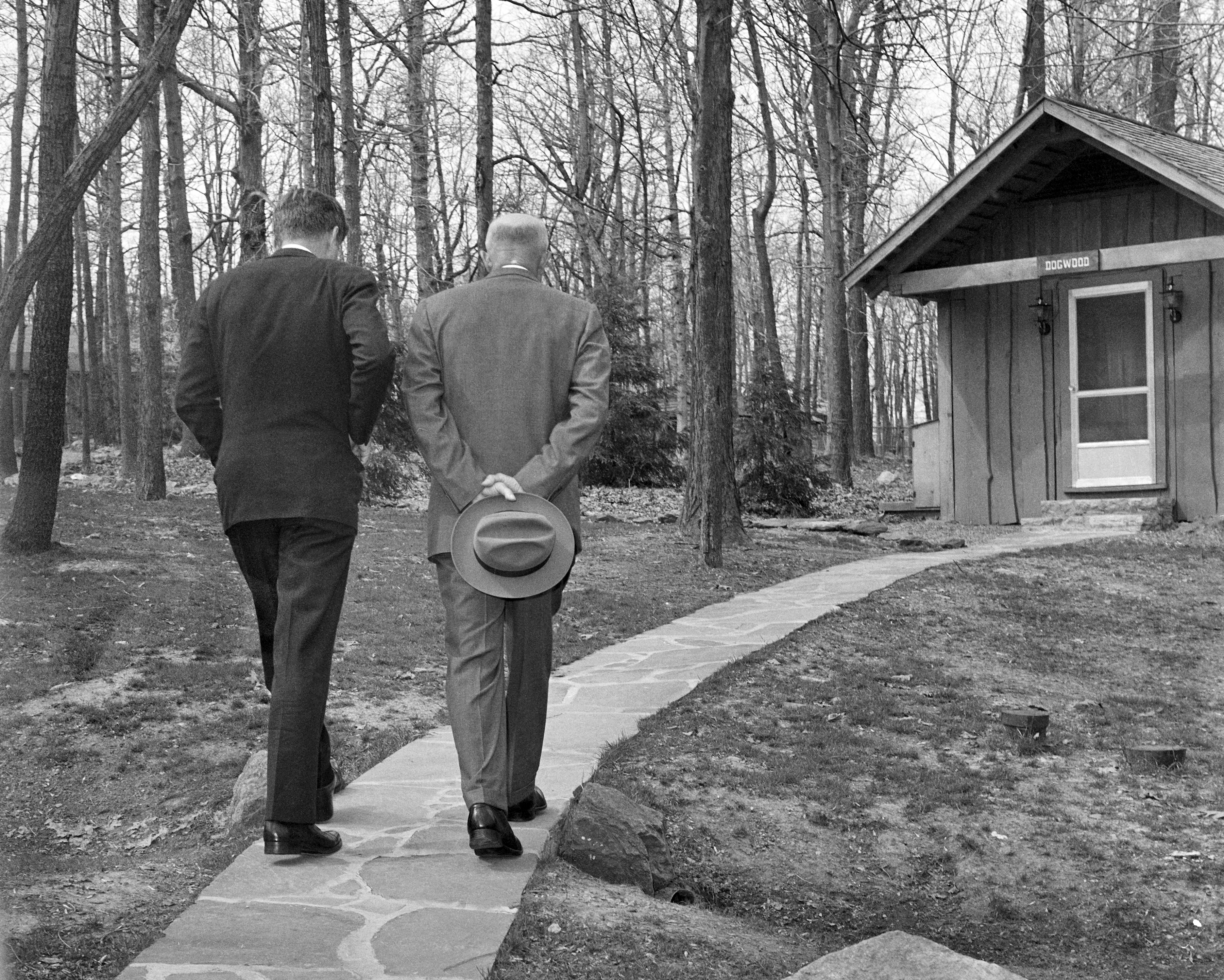 With their heads bowed, President John F. Kennedy, left, walks along a path at Camp David near Thurmont, Md., with former President Dwight D. Eisenhower, April 22, 1961, as the two met to discuss the Bay of Pigs invasion. The photo was shot between the legs of a Secret Service agent. (AP Photo/Paul Vathis)