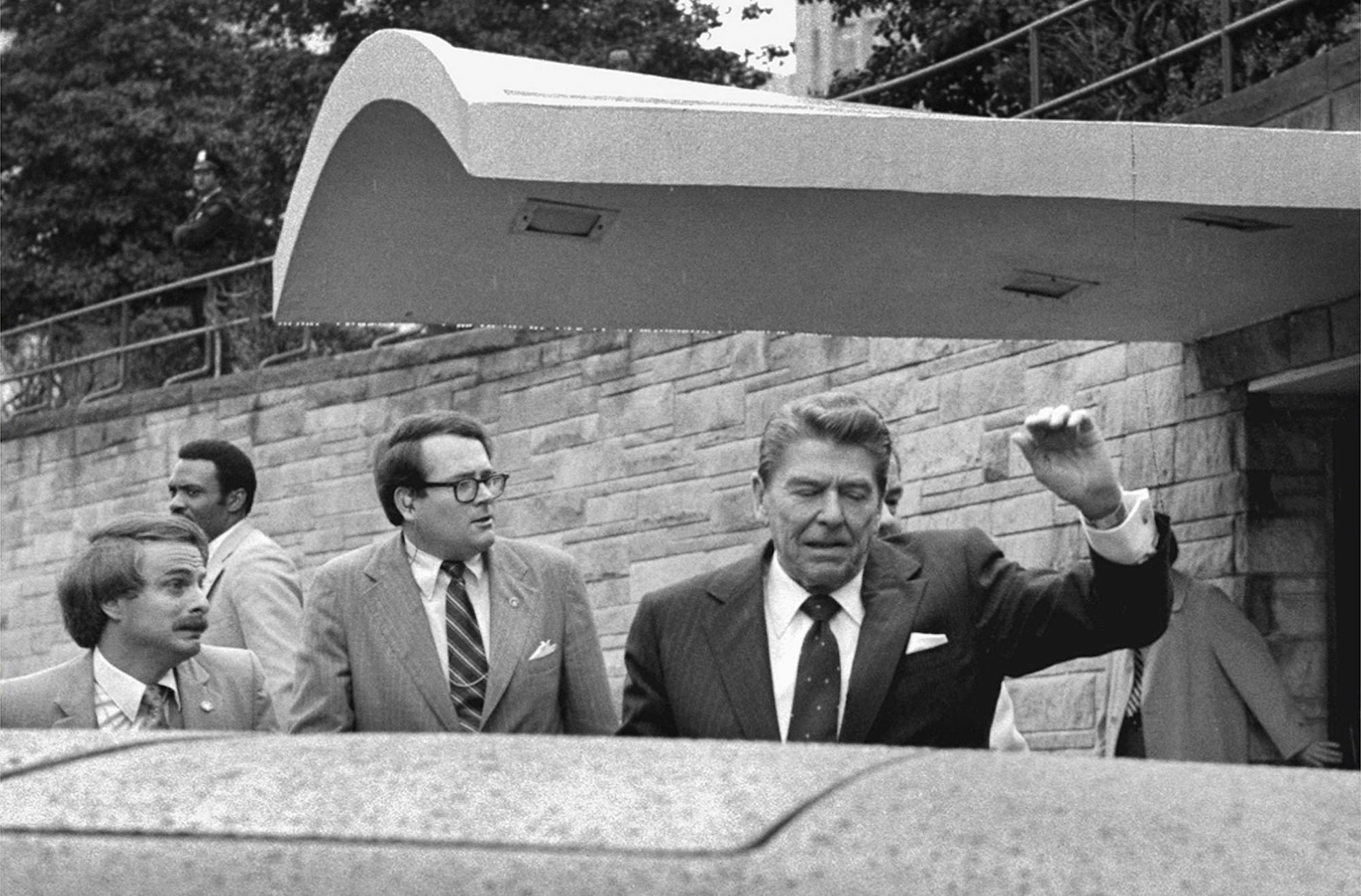 U.S. President Ronald Reagan looks to his left and holds up his left arm as a secret service agent places a hand on his shoulder and pushes the President into his limousine after he was shot leaving a Washington hotel, Monday, March 30, 1981. (AP Photo/Ron Edmonds)