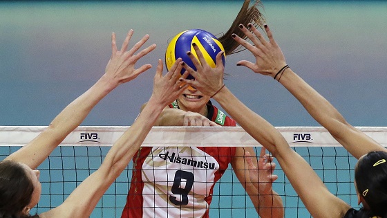 Female volleyball players blocking ball being hit over a net